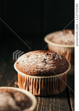 Chocolate muffins with powdered sugar on a black background. Still life close up. Dark moody. Food photo. 112734160