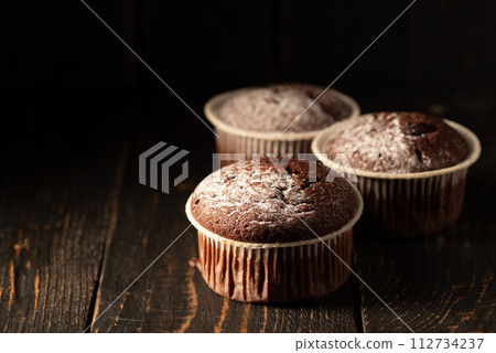 Chocolate muffins with powdered sugar on a black background. Still life close up. Dark moody. Food photo. 112734237