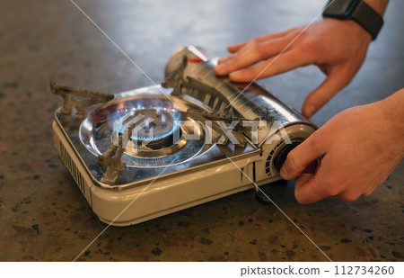Active lifestyle. A man's hand turns on a portable gas stove. An alternative source for cooking at home during a power outage. Active lifestyle. A man's hand turns on a portable gas stove. An alternative source for cooking at home during a power outage. 112734260
