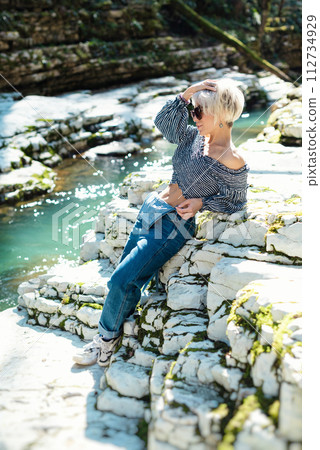 a beautiful sexy girl in nature among a mountain river and a rocky canyon in a denim jumpsuit smiles cheerfully and enjoys life on vacation in the summer 112734929
