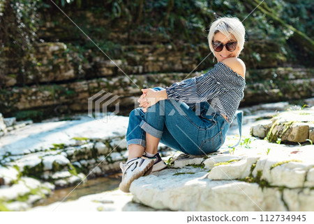 a beautiful sexy girl in nature among a mountain river and a rocky canyon in a denim jumpsuit smiles cheerfully and enjoys life on vacation in the summer 112734945