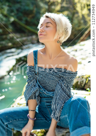 a beautiful sexy girl in nature among a mountain river and a rocky canyon in a denim jumpsuit smiles cheerfully and enjoys life on vacation in the summer a beautiful sexy girl in nature among a mountain river and a rocky canyon in a denim jumpsuit smiles cheerfully and enjoys life on vacation in the summer 112734949