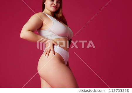 Cropped portrait of woman, model plus size posing in lingerie against pink studio background. Overweight girl looks confident. Cropped portrait of woman, model plus size posing in lingerie against pink studio background. Overweight girl looks confident. 112735228