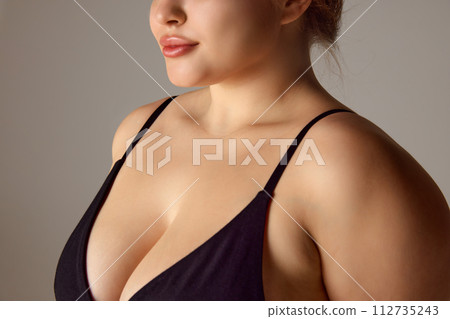 Cropped portrait of woman, plus size model with well-kept skin on neckline zone against grey studio background. Cropped portrait of woman, plus size model with well-kept skin on neckline zone against grey studio background. 112735243