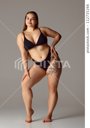 Full length portrait of young chubby woman posing in lingerie against grey studio background. Self-expression. Full length portrait of young chubby woman posing in lingerie against grey studio background. Self-expression. 112735266