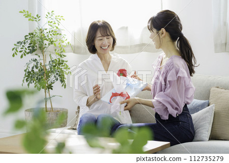 母親節：一位年輕女子在家中客廳送給母親康乃馨和禮物 112735279