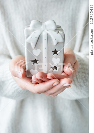 The image shows hands delicately holding the figurine as a gift, decorated with stars and hearts, tied with a bow. The background is soft and neutral tones. The image shows hands delicately holding the figurine as a gift, decorated with stars and hearts, tied with a bow. The background is soft and neutral tones. 112735455
