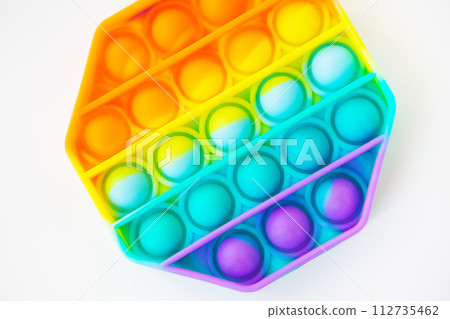 A colorful pop it fidget toy against a white background. The hexagonal toy has vibrant rainbow colors and bubbles to pop. 112735462