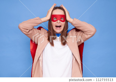 Unhappy displeased woman wearing superhero costume standing isolated over blue background crying with despair holding head suffering having bad feelings Unhappy displeased woman wearing superhero costume standing isolated over blue background crying with despair holding head suffering having bad feelings 112735513