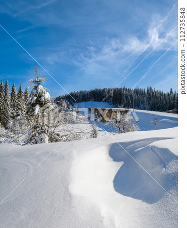 Stone viaduct (arch bridge) on railway through mountain snowy fir forest. Snow drifts  on wayside and hoarfrost on trees and electric line wires. 112735848