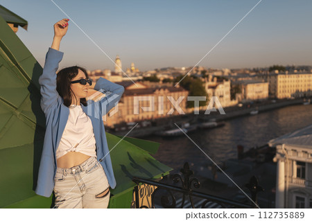 Young happy woman in jeans and blue jacket relaxing on rooftop in St Petersburg 112735889