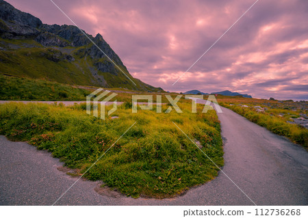 The road along mountains with a cloudy sky during sunset. Leisure area Flakstad, Lofoten Islands, Norway 112736268