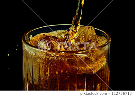 Soda, coke, dark beer pouring from bottle into glass with ice cubes against black background 112736713