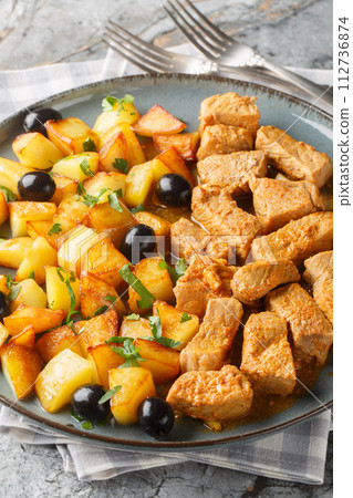 Rojoes a moda do Minho typical Portuguese pork dish with fried potato and olive closeup on the plate. Vertical Rojoes a moda do Minho typical Portuguese pork dish with fried potato and olive closeup on the plate. Vertical 112736874