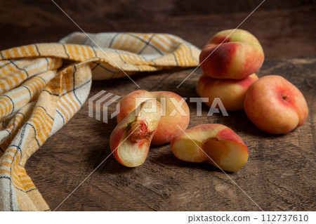 Half and several whole saturn peaches or flat peaches on wooden background with yellow kitchen towel.. Half and several whole saturn peaches or flat peaches on wooden background with yellow kitchen towel.. 112737610