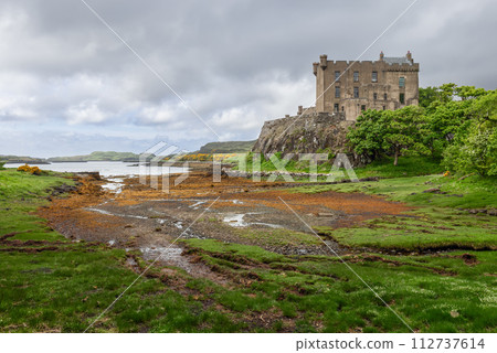 Dunvegan Castle stands on a rugged cliff overseeing a loch with shores painted in greens and auburns Dunvegan Castle stands on a rugged cliff overseeing a loch with shores painted in greens and auburns 112737614
