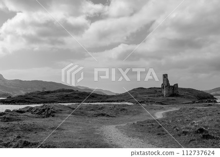 Black and white serene landscape with Ardvreck Castle ruins set against Scotland's rugged terrain 112737624