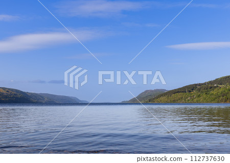 Loch Ness calm waters lead to the horizon, surrounded by green hills under a vast Scottish sky Loch Ness calm waters lead to the horizon, surrounded by green hills under a vast Scottish sky 112737630