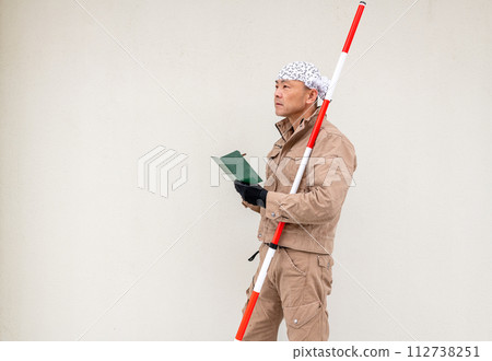 A civil engineering man is writing in a memo pad while holding a surveying pole under his arm. A civil engineering man is writing in a memo pad while holding a surveying pole under his arm. 112738251