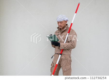 一名土木工程人員腋下夾著一根測桿，正在記事本上寫字。 112738254