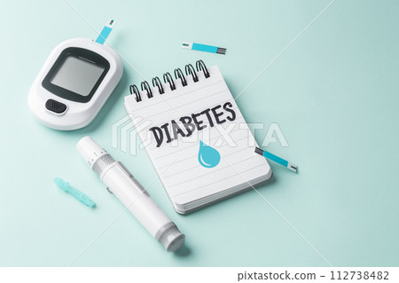 Diabetes concept with notepad and blood glucose sugar meter on light green background, copy space 112738482