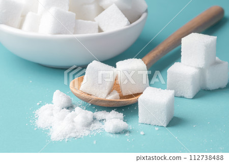 Sugar cube on wood spoon, closeup on blue background Sugar cube on wood spoon, closeup on blue background 112738488