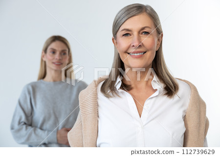 Confident mature woman standing, her daughter behind her Confident mature woman standing, her daughter behind her 112739629