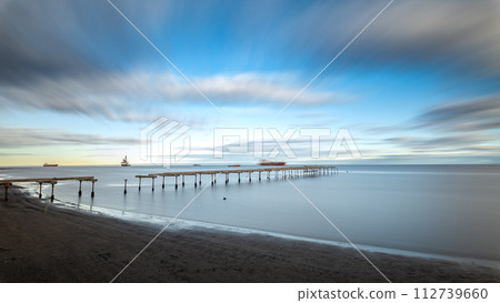 Serene seascape with long pier under a dynamic sky Serene seascape with long pier under a dynamic sky 112739660