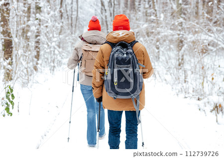 Two people walking on a winter forest with scandinavian sticks Two people walking on a winter forest with scandinavian sticks 112739726