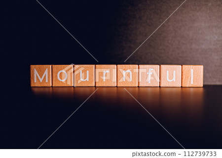 Wooden blocks form the text "Mournful" against a black background. 112739733