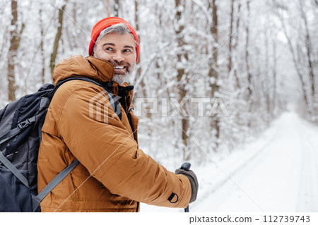 Man having a walk with scandinavian sticks in a snowy forest 112739743