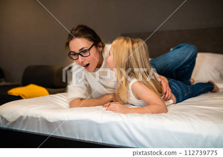 Cute little girl whispering secret to mother ear while resting in hotel room 112739775