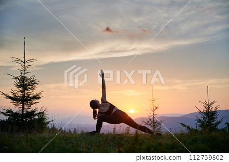 Woman practicing yoga outdoors in the mountains in a serene, natural setting. Female performing yoga pose, with backdrop of beautiful mountain landscape at sunrise or sunset. Woman practicing yoga outdoors in the mountains in a serene, natural setting. Female performing yoga pose, with backdrop of beautiful mountain landscape at sunrise or sunset. 112739802