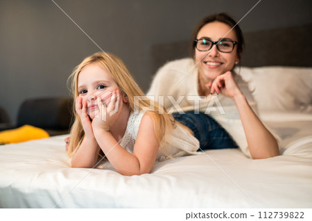 Mother and child girl in bedroom cuddling on cozy warm comfortable bed in hotel room Mother and child girl in bedroom cuddling on cozy warm comfortable bed in hotel room 112739822