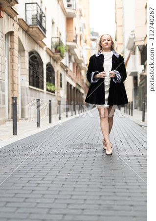 Happy woman in stylish dress walks along cobblestone street Happy woman in stylish dress walks along cobblestone street 112740267