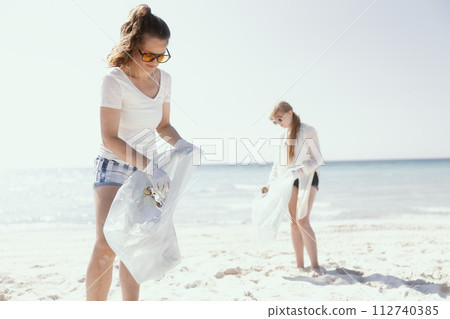 concerned female volunteers on ocean coast collecting garbage concerned female volunteers on ocean coast collecting garbage 112740385