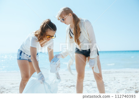 smiling women volunteers on beach collecting garbage 112740393