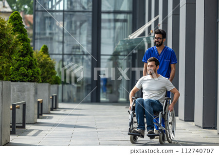 Brunette male nurse rolling a wheelchair with a patient 112740707