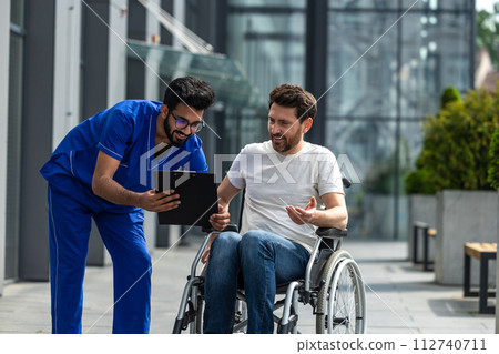 Man sitting in a wheelchair and discussing something with male nurse Man sitting in a wheelchair and discussing something with male nurse 112740711