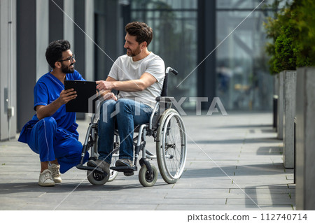 Man sitting in a wheelchair and discussing something with male nurse 112740714