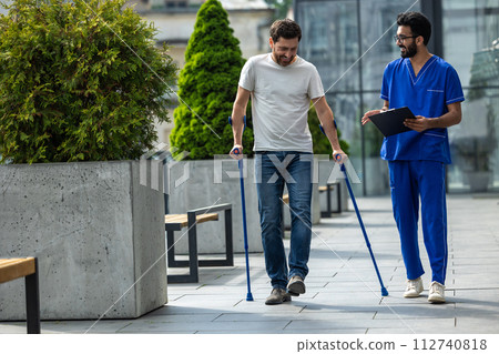 Man with crutches and a male nurse talking friendly on a walk 112740818