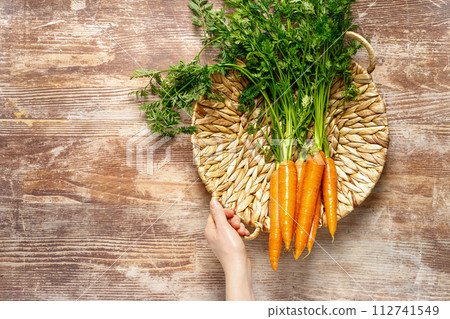 Fresh organic farmer carrots bunch with green tops in a basket on wooden rustic kitchen table, top down view Fresh organic farmer carrots bunch with green tops in a basket on wooden rustic kitchen table, top down view 112741549