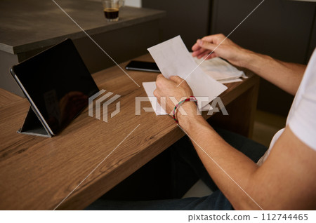 Close-up man sitting in his home office with bills in hands and paying it online over digital tablet. E-banking concept. 112744465