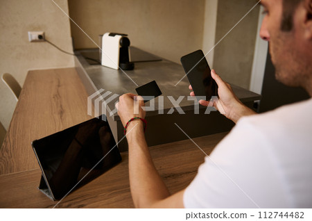 Rear view of young adult man holding a blank black credit card and smartphone with empty mockup digital screen Rear view of young adult man holding a blank black credit card and smartphone with empty mockup digital screen 112744482