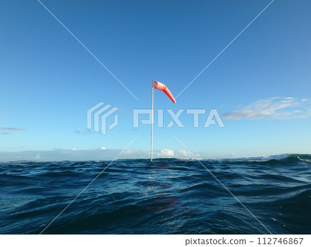 Flag pole with wind sock rises above the wavy waters of Waikiki Flag pole with wind sock rises above the wavy waters of Waikiki 112746867
