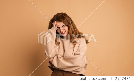 Frustrated woman suffering from headache in brown studio Frustrated woman suffering from headache in brown studio 112747475