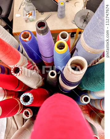 Bobbins filled with colorful threads adorn the sewing table, ready to weave vibrant patterns into fabric Bobbins filled with colorful threads adorn the sewing table, ready to weave vibrant patterns into fabric 112747674