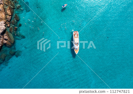 Aerial top down view of a swimming tourists and yacht anchored in the turquoise sea 112747821