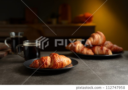 Fresh baked croissants and black coffee on a kitchen table. 112747958
