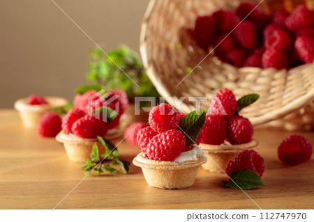 Tartlets with fresh raspberries and mint on a wooden table. Tartlets with fresh raspberries and mint on a wooden table. 112747970